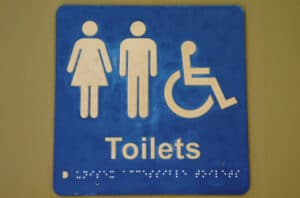 ADA-compliant restroom sign with male, female, and wheelchair symbols and Braille text.