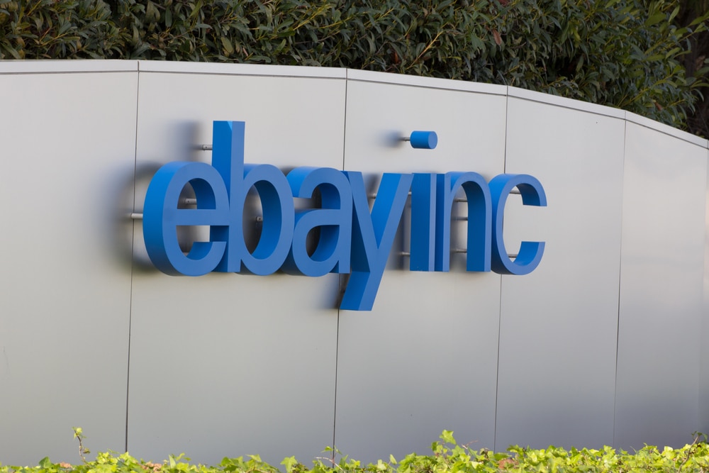 Large blue "ebay inc." logo on a gray metal wall with bushes below.