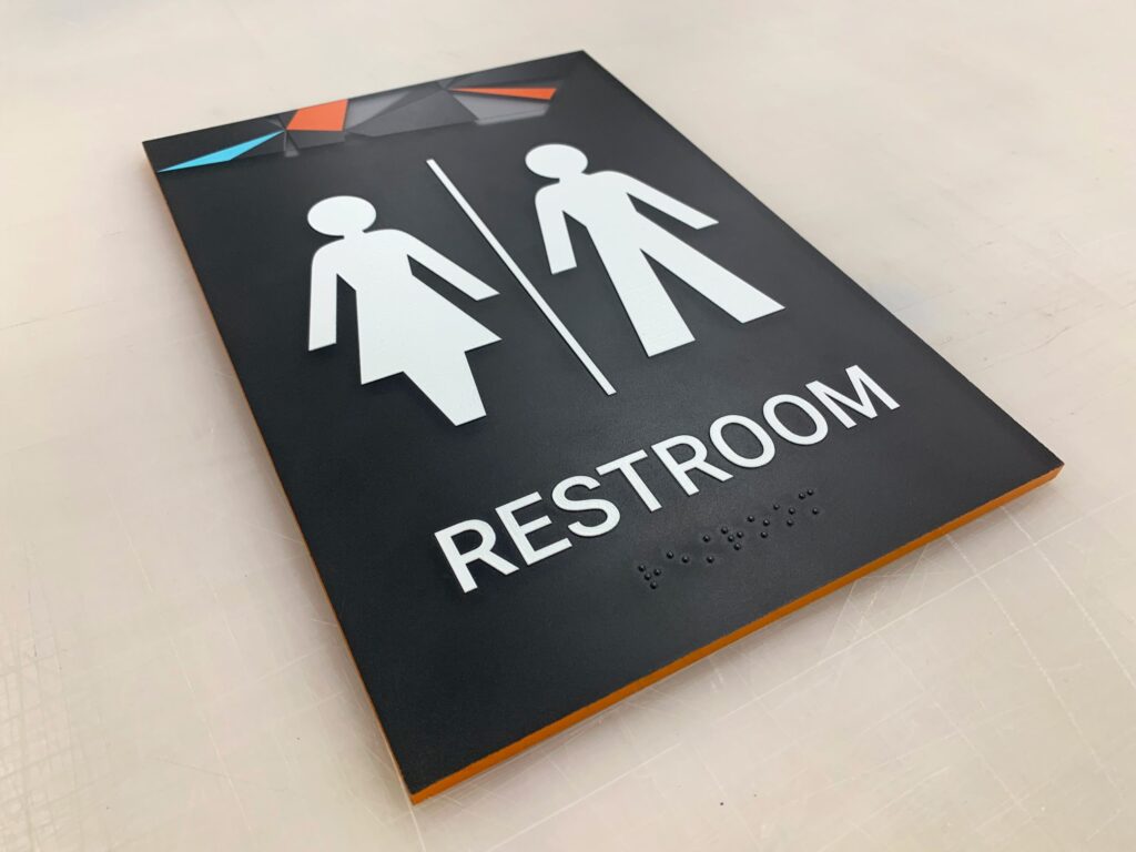 ADA-compliant unisex restroom sign with high contrast white symbols for male, female, and wheelchair accessibility on a black background.