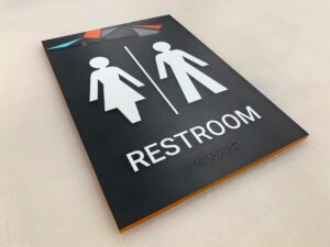 ADA-compliant unisex restroom sign with high contrast white symbols for male, female, and wheelchair accessibility on a black background.