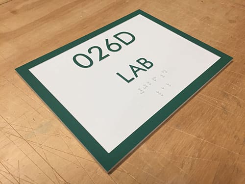 Durable interior sign with a green border and white background, indicating "026D LAB" with room numbering and tactile Braille for accessibility, suggesting a long-lasting and compliant design.