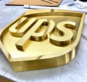 Elegant gold-toned dimensional metal logo sign for UPS, showcasing the iconic shield and lettering in a solid, substantial design.
