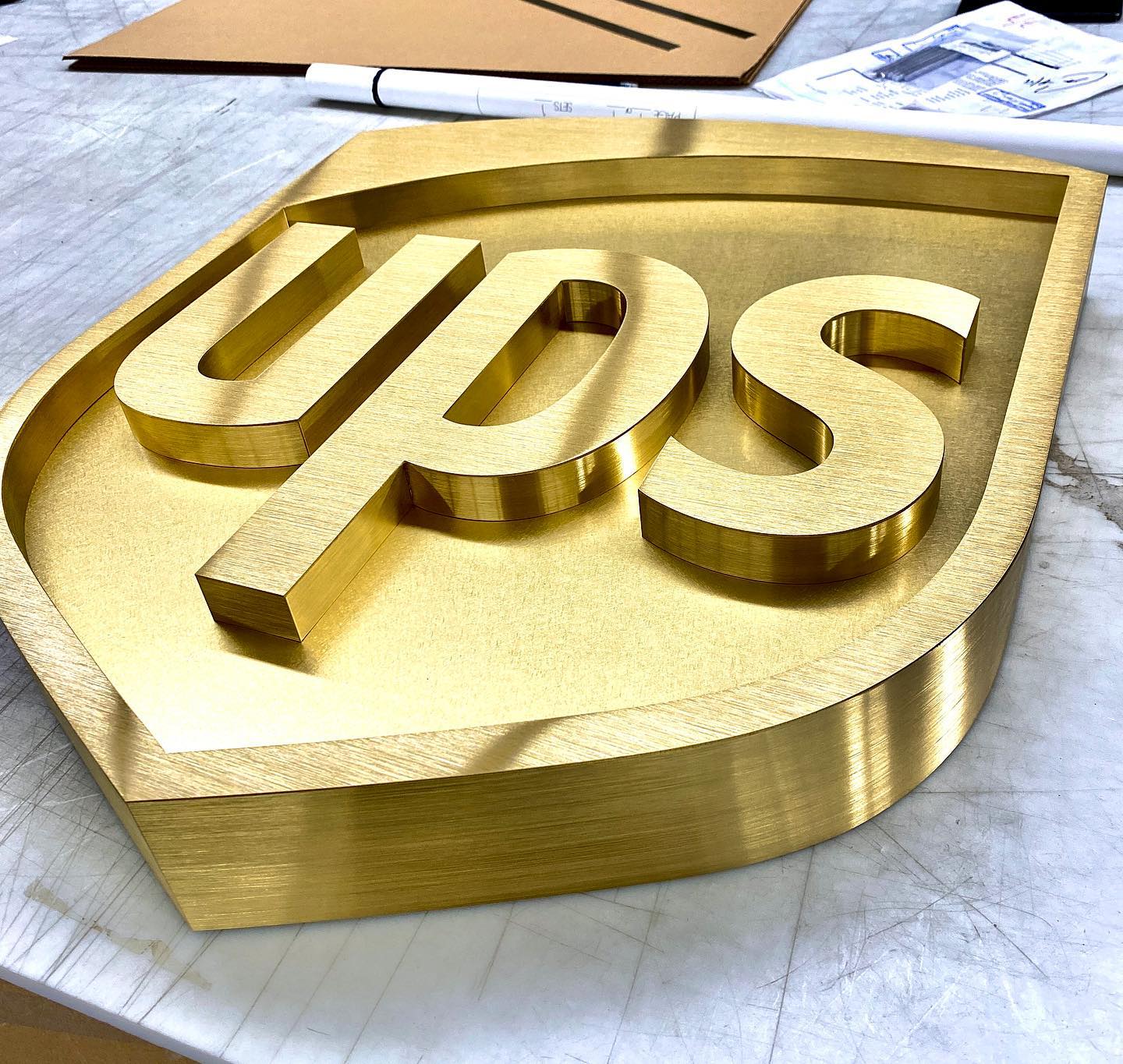 Elegant gold-toned dimensional metal logo sign for UPS, showcasing the iconic shield and lettering in a solid, substantial design.