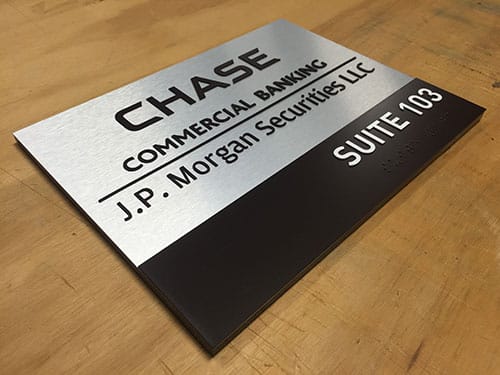 Silver and black vandal-resistant business sign for Chase Commercial Banking and J.P. Morgan Securities LLC, indicating Suite 103 with tactile Braille.