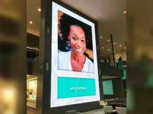 Bright, vertical LED welcome sign in a dental office, featuring a smiling woman with dark skin and natural hair, and the word "welcome" in a teal script font above the text "INNOVATIVE DENTAL"