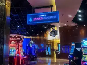 Bright digital welcome sign hanging above the entrance area of Jamul Casino, featuring the casino's name in illuminated blue letters and a water droplet logo, with slot machines and a restaurant sign visible in the background.