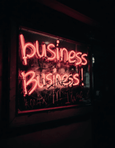 A red neon sign displaying 'business Business!' with the lower part appearing scratched and defaced, illustrating how traditional business signage can be susceptible to vandalism and damage, unlike vandal-resistant options.